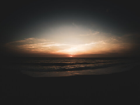 Dark cinematic sunset over a moody ocean with waves crashing on a sandy beach at dusk under a vignette sky