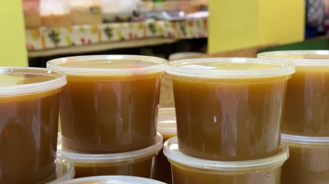 Close-up honey jars on counter warm amber honey in clear plastic containers stacked on cloth market display glossy texture visible