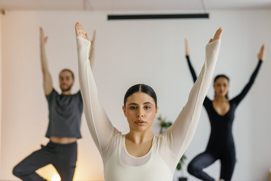 Woman practice yoga in Vrksasana pose with other blurred man and woman