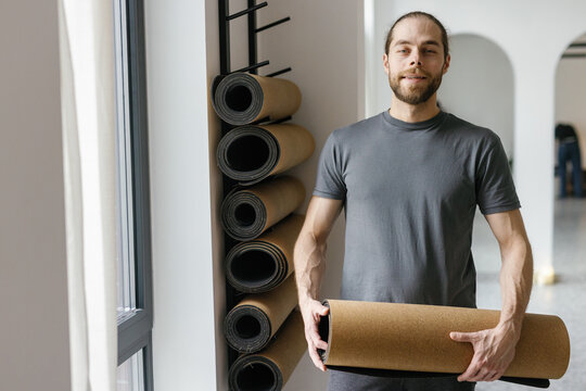Portrait of young sportsman holding sports carpet in fitness studio