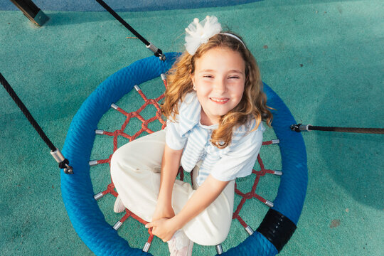 Girl sitting on circular climbing net looking up