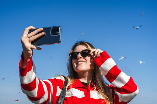 Woman taking selfies with kites in the sky in the background