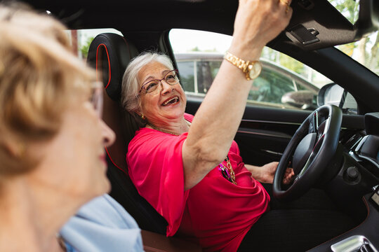 Senior woman laughing driving car with friend enjoying road trip