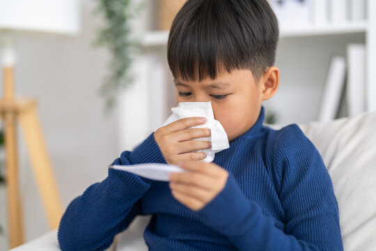 Sick asian boy child wiping runny nose with tissue and checking a digital thermometer for high fever temperature, Concept of flu symptoms, child health care, rsv, influenza and bronchitis illness