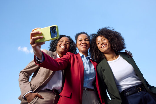 Three fashionable women pose for a selfie outside. 