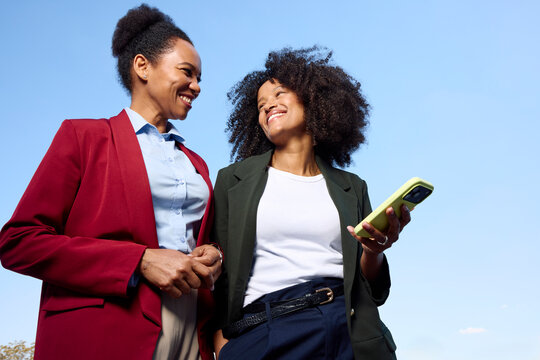 Stylish women stand against a clear sky.