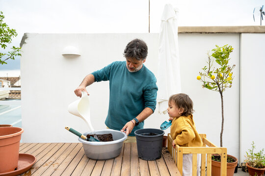 Father And Baby Watering Soil Together On Terrace