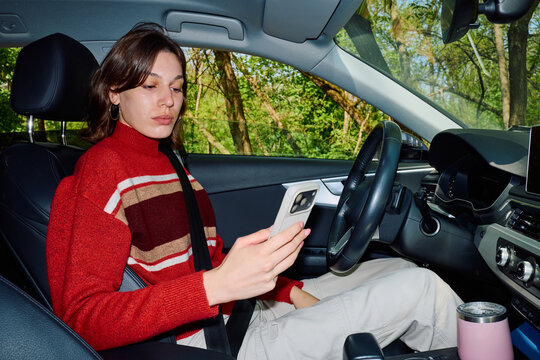 Woman waits in her car, looking at a mobile phone