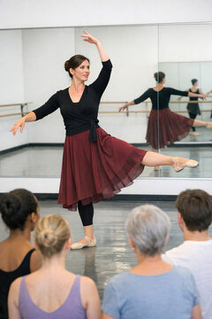A woman dancing ballet, instructing others in a classroom setting.