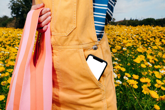 Person Holds Phone in Pocket Near Yellow Flowers in a Field