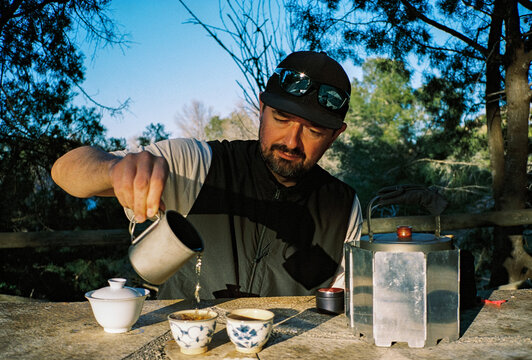 Young man pouring tea into bowls while sitting at a table outdoors