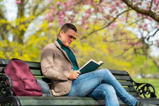 Man reading book in park on bench