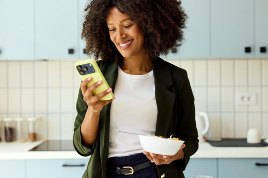 Woman smiles while using smartphone in the kitchen