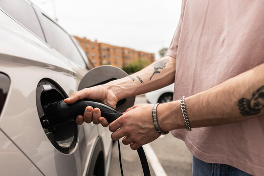 Person plugging charging cable into electric vehicle