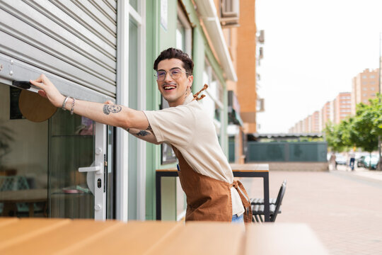Happy young man opening store shutter in morning
