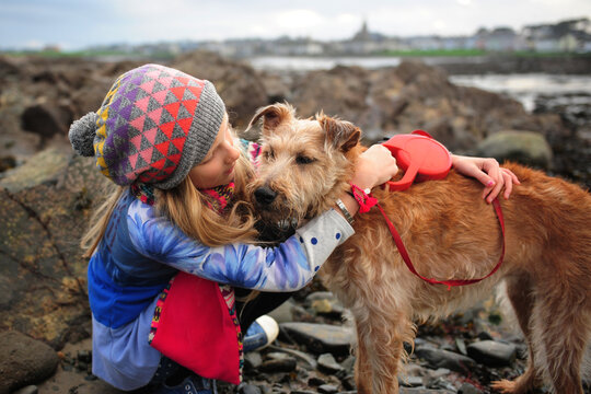 A girl hugs her dog at the beach in winter