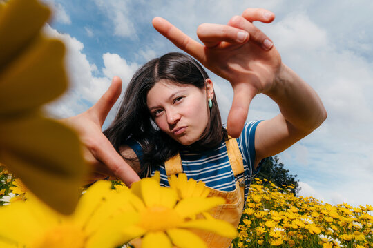 Girl Makes a Frame With Her Hands in a Flower Field on a Sunny Day