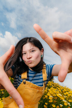 Girl Makes a Frame With Her Hands in a Flower Field on a Sunny Day