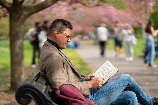 Man reading book in park on bench