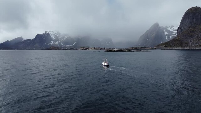 Small fishing boat crossing choppy northern coastal waters toward snow-dusted rocky mountains