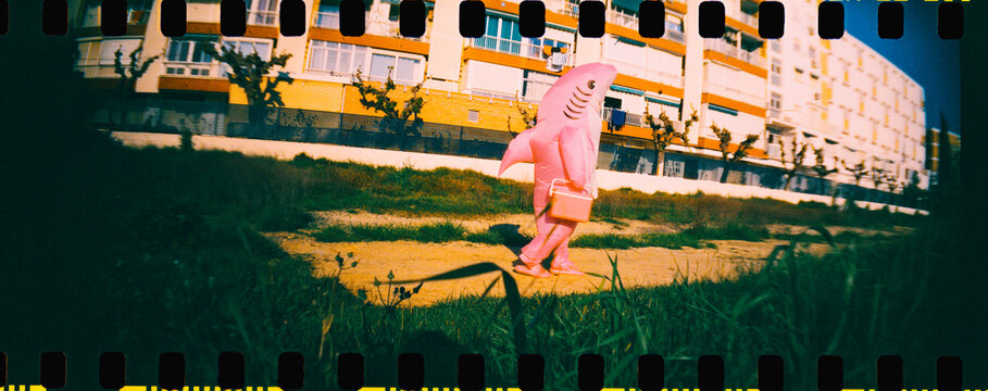 a man in a pink shark costume walking with a cooler, 35mm film