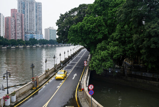 Yellow car drives along river road in urban setting 