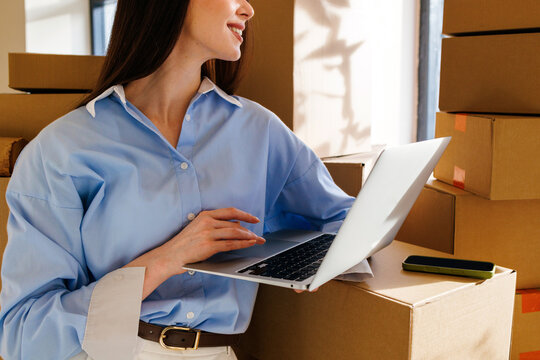 Businesswoman using laptop among cardboard boxes indoors