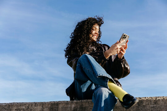Curly haired woman smiling using smartphone