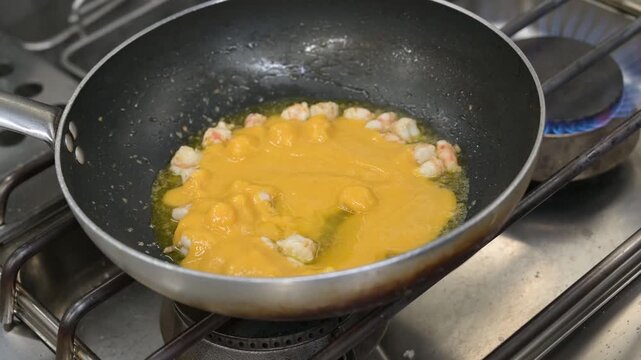 preparazione in una padella nella cucina di un ristorante di un sughetto con mazzancolle frescehe ed un sughetto di pomodorini gialli