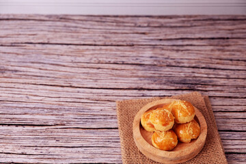 Fototapeta premium Kue Nastar or Golden pastries rest in a wooden bowl. Bowl sits atop burlap on aged wood. Warm tones evoke comfort and homemade charm. Ideal for food blogs, bakery ads, or cozy lifestyle content