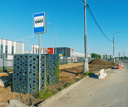 Bus stop and roadside construction near industrial buildings under clear sky