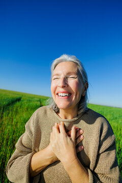 Grey haired woman smiling with gratitude in meadow