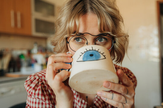 Woman drinking coffee from mug with eye illustration in cozy kit