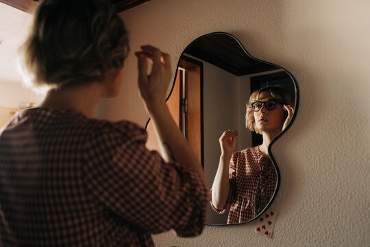 Woman adjusting eyeglasses while looking in mirror at home