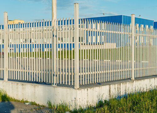 White metal security fence around blue industrial building under clear sky