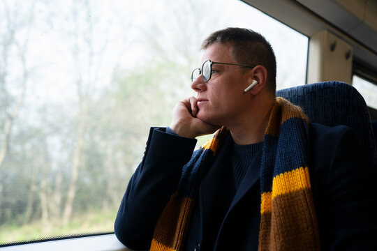 Man with earbuds looking through train window