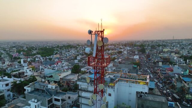 Dynamic drone reveal of mobile network tower over crowded rooftops.