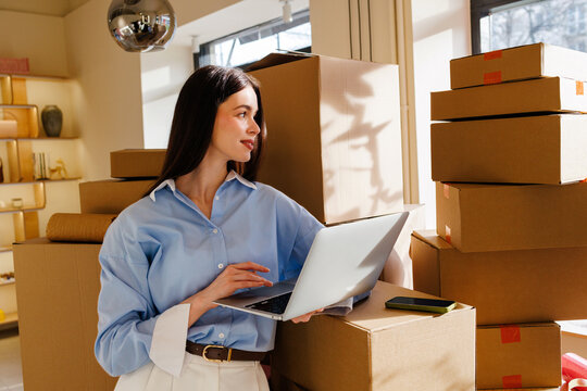 Woman using laptop in small business with cardboard boxes 