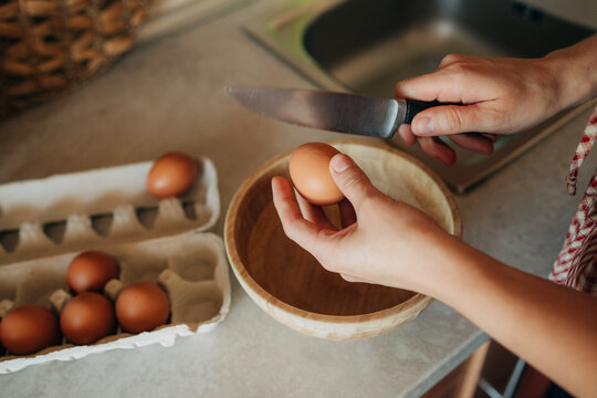 Hands cracking egg with knife over bowl in kitchen