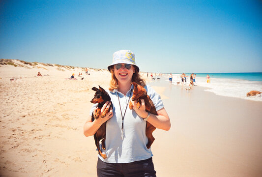 Woman Holds Two Dogs on the Beach During a Sunny Day in Summer