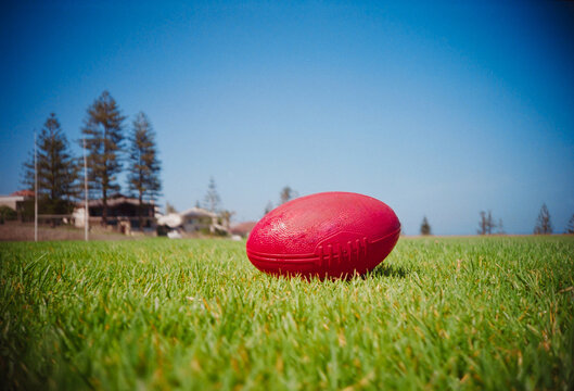 Red AFL Footie Ball on Green Grass Field Under Clear Blue Sky