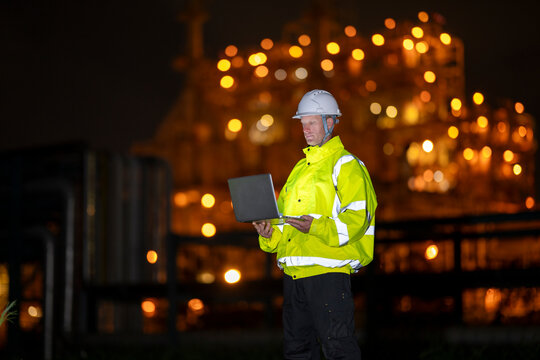 Engineer working on laptop at industrial plant at night