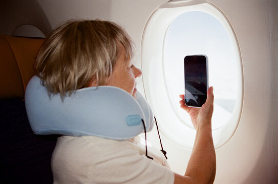 Grandma uses phone while sitting by the airplane window.
