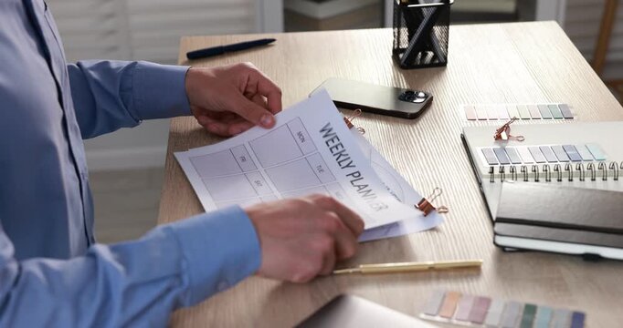 Man using weekly planner at wooden desk indoors, closeup