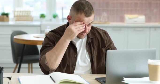 Workaholic. Overwhelmed man working with laptop at wooden desk in kitchen, camera moving forward