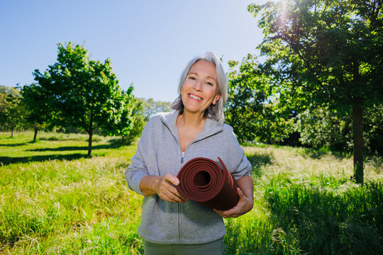 Senior woman holding rolled yoga mat enjoying outdoor workout