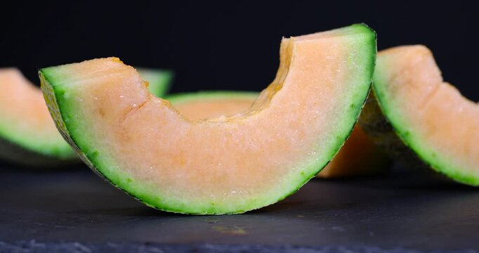  sliced sweet melon, fresh orange melon with a moist surface and textured peel on a black table under soft light with an authentic look and vibrant color.