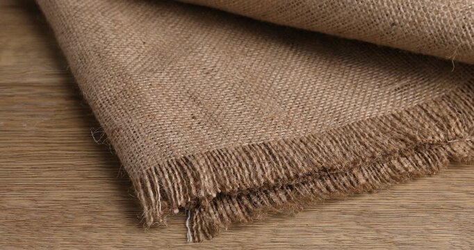 Woman with folded burlap fabric at wooden table, closeup