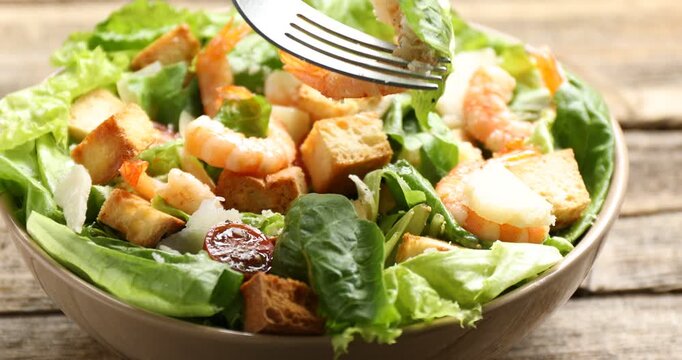 Eating delicious Caesar salad with shrimps at wooden table, closeup