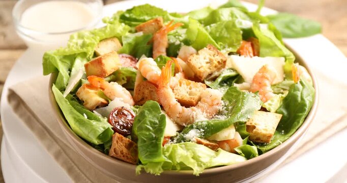 Delicious Caesar salad with shrimps in bowl on table, closeup